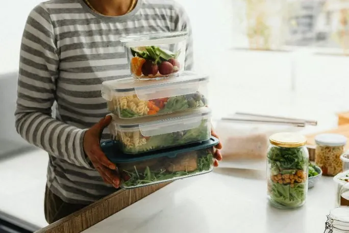 Person holding stacked meal prep containers filled with salads and vegetables.