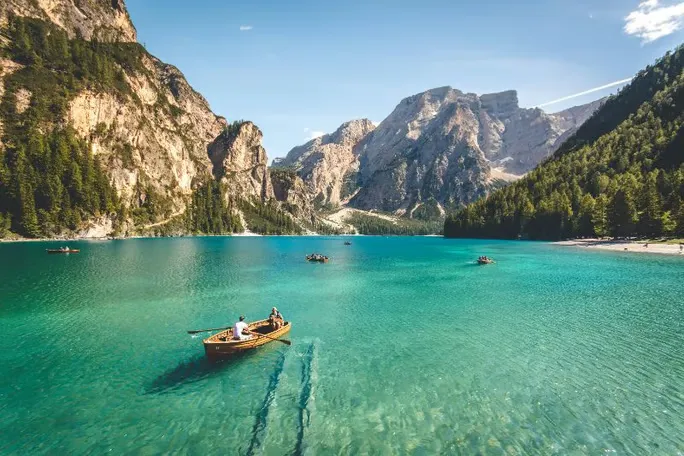 Scenic lake with turquoise water and wooden rowboats surrounded by mountains.