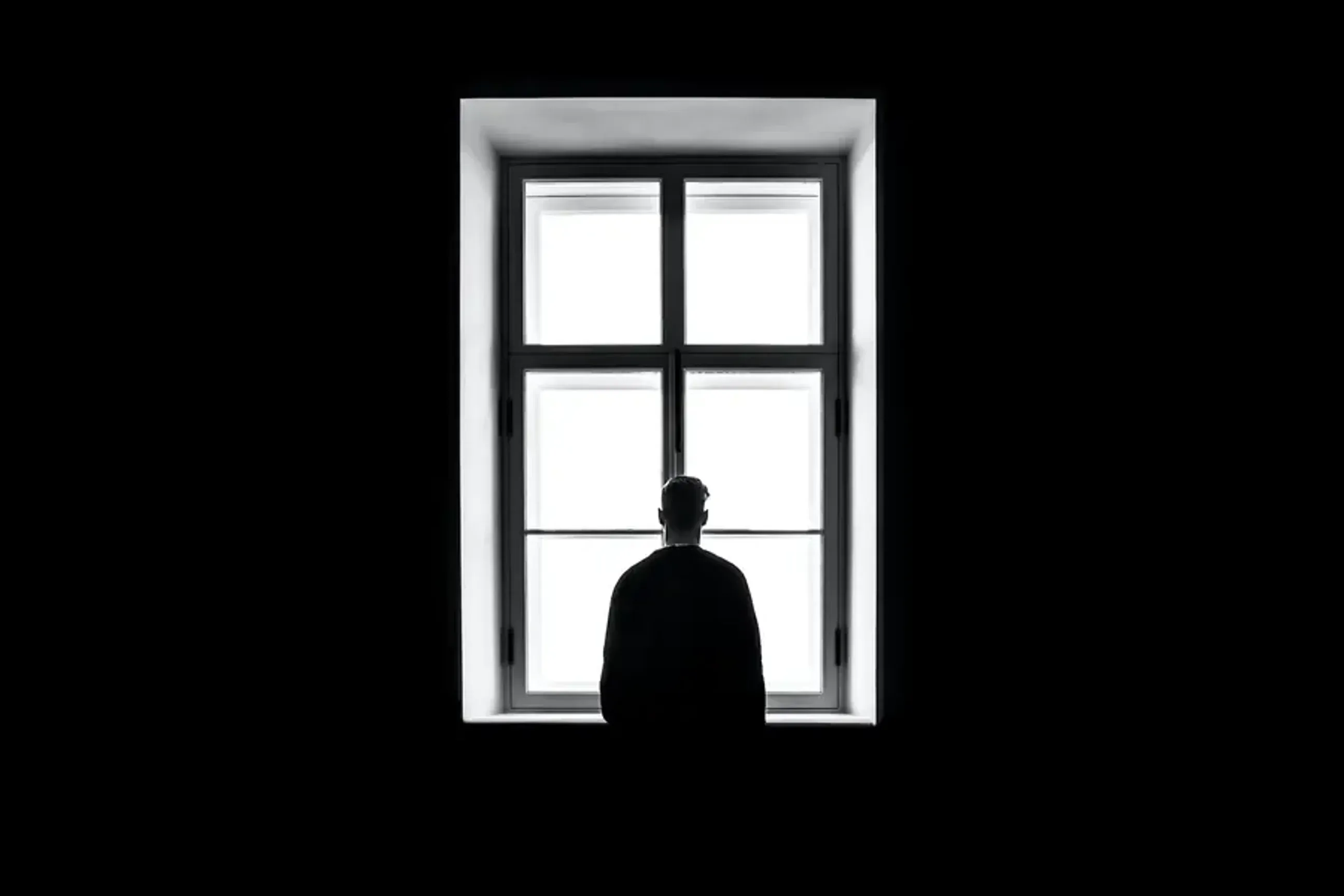 Silhouette of a person sitting in front of a bright window in a dark room.